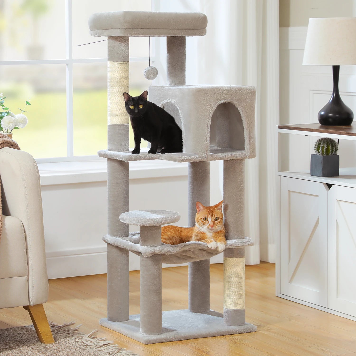 Two cats on a multi-level cat tree in a living room setting.