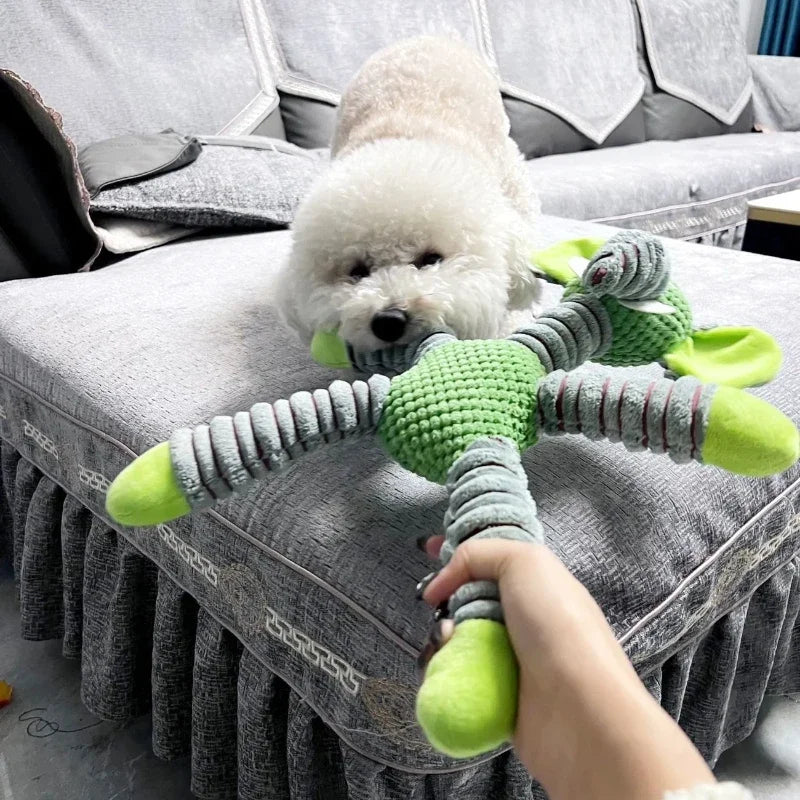 White dog playing with a green and gray toy on a gray couch.