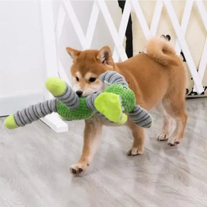 Dog playing with a toy resembling a green lizard on a light wooden floor.